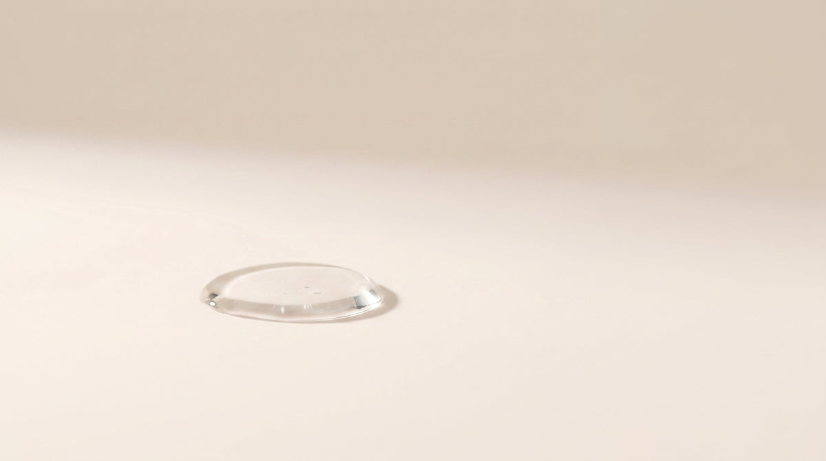 Minimalistyczna kompozycja z przezroczystą kroplą serum symbolizującą lekką formułę kosmetyczną